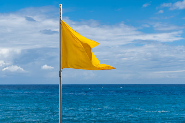 Yellow storm warning flag flying on a pole near the ocean under a clear sky.