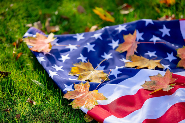 American flag laid on grass with autumn leaves, reflecting respectful care at Kengla Flag Co.