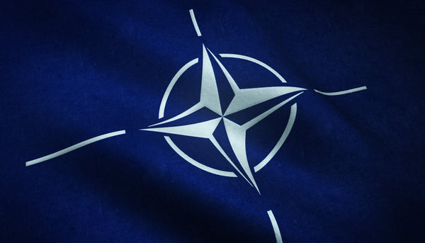 Close-up of a NATO flag waving, featuring a white compass rose on a dark blue fabric.