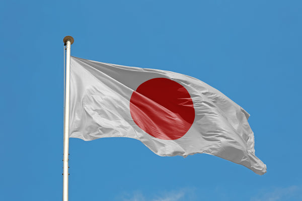 Japan flag waving on a flagpole against a clear blue sky.