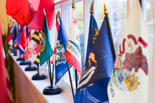 Row of miniature U.S. state flags on stands displayed along a windowsill at Kengla Flag Co.