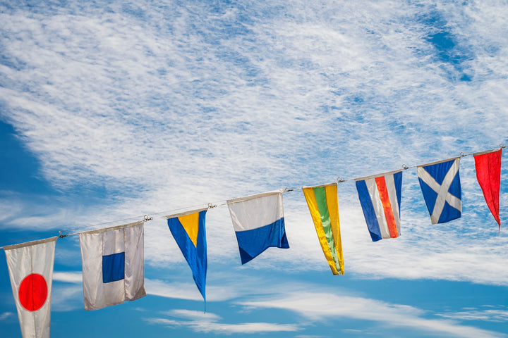 Colorful maritime alphabet signal flags strung against a bright blue sky.