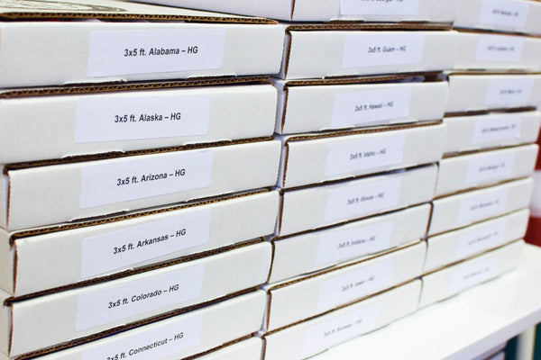 Stacked boxes labeled with state flags and sizes organized for inventory at Kengla Flag Co warehouse.