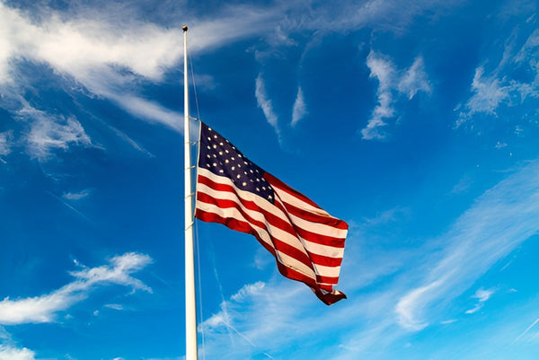 American flag flying at half-staff against a bright blue sky, displayed by Kengla Flag Co.