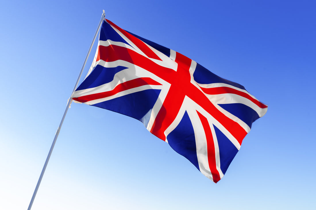 Kengla Flag Co. United Kingdom flag flying from a white pole against a bright blue sky.