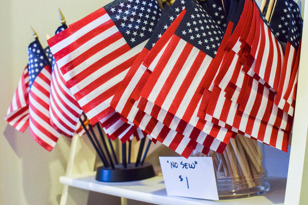 Cluster of small American flags on sticks displayed on a white shelf at Kengla Flag Co.