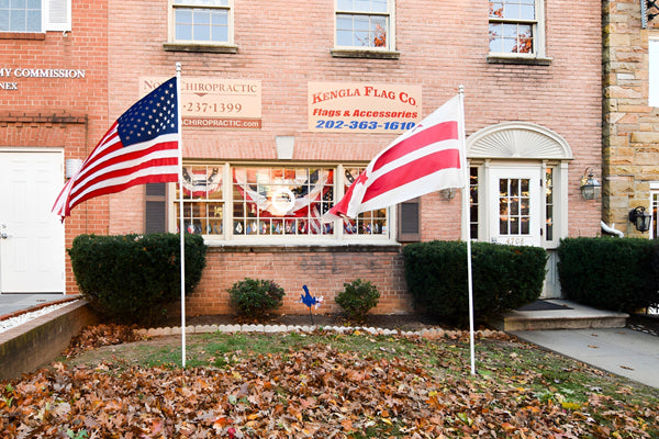 American and red-white flags flying outside Kengla Flag Co. storefront with flag shop sign.